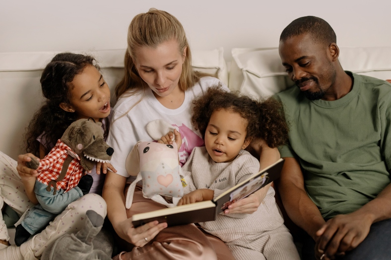 A mum, dad and two daughters read a story book together