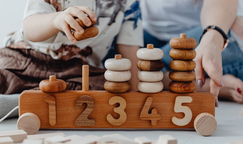 A mum and adopted child playing with a wooden toy with numbers one to five